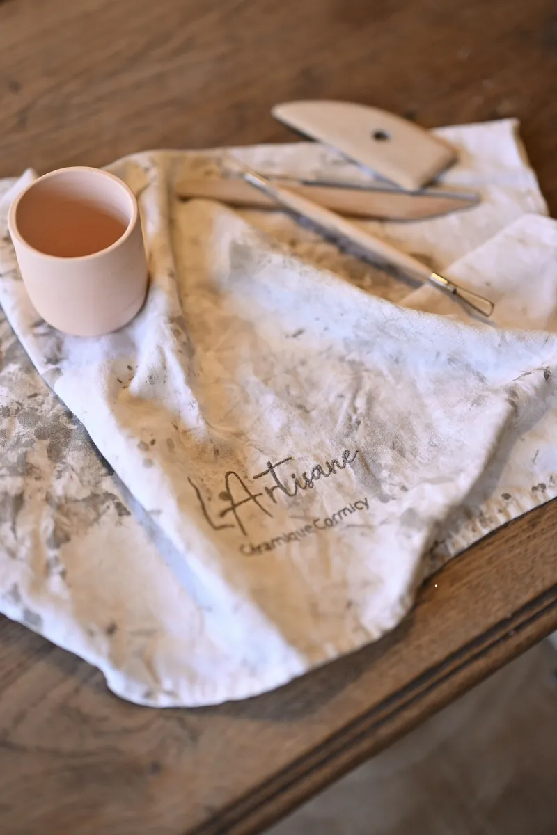 Tasse en céramique et outils de potier sur un torchon L'Artisane